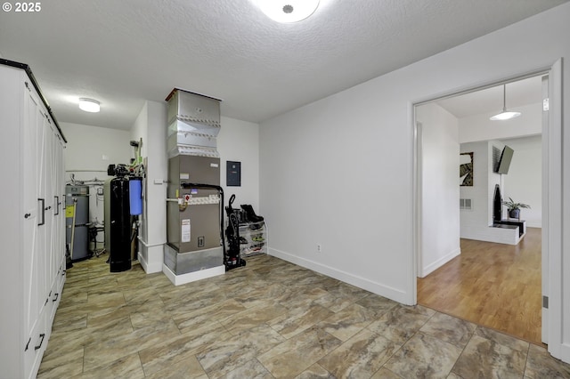 basement featuring heating unit, baseboards, a textured ceiling, light stone finish flooring, and electric panel