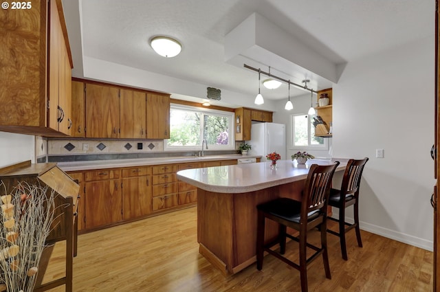 kitchen with freestanding refrigerator, brown cabinets, light wood-style floors, decorative backsplash, and a peninsula