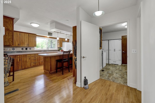 kitchen featuring brown cabinets, light countertops, freestanding refrigerator, light wood-style floors, and a sink
