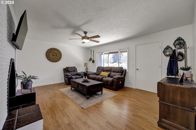 living room featuring ceiling fan, light wood-style flooring, baseboards, and a textured ceiling
