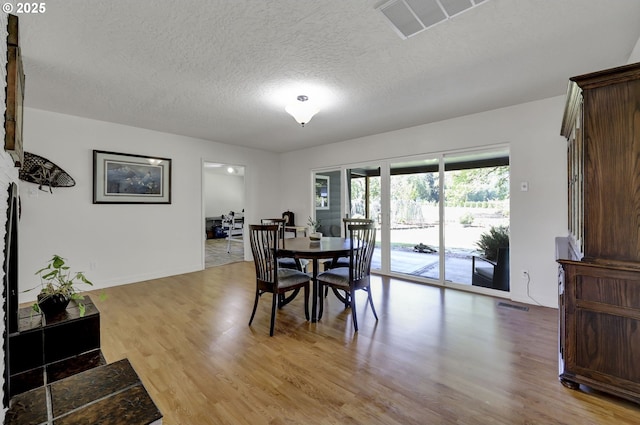 dining room featuring light wood-style flooring, a textured ceiling, and baseboards