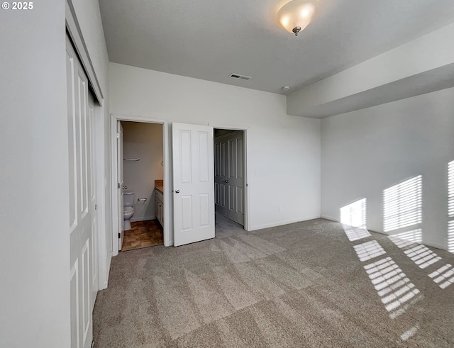 unfurnished bedroom with visible vents, baseboards, carpet flooring, a closet, and ensuite bath