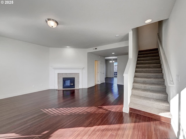 unfurnished living room with wood finished floors, baseboards, visible vents, a tile fireplace, and stairs