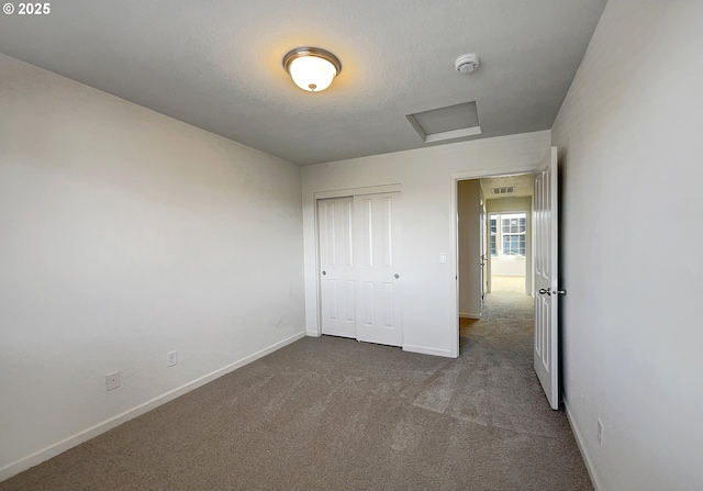 unfurnished bedroom featuring visible vents, baseboards, attic access, carpet flooring, and a closet