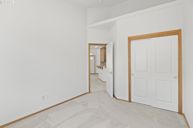 unfurnished bedroom with baseboards, light carpet, and a closet