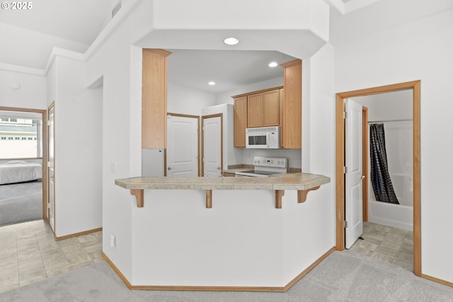 kitchen with baseboards, light carpet, a breakfast bar, and white appliances