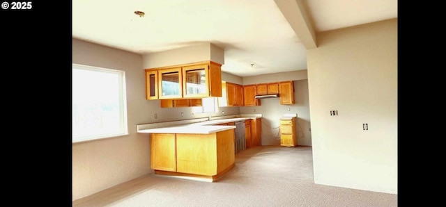 kitchen featuring light colored carpet, brown cabinets, light countertops, a peninsula, and under cabinet range hood