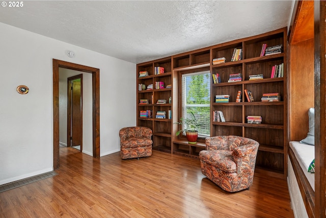 living area with baseboards, a textured ceiling, and wood finished floors