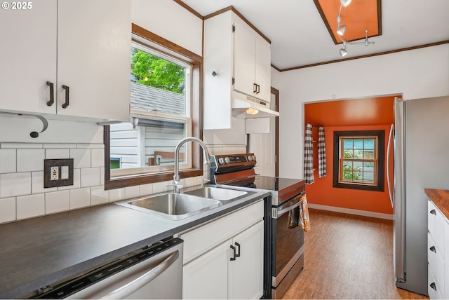 kitchen with appliances with stainless steel finishes, dark countertops, a sink, white cabinets, and under cabinet range hood