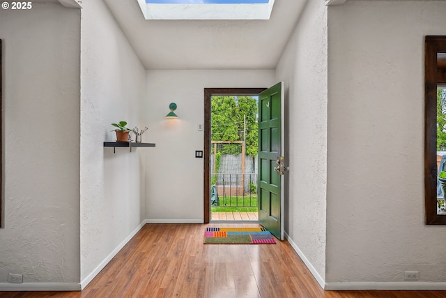 interior space featuring baseboards, a skylight, a textured wall, and wood finished floors