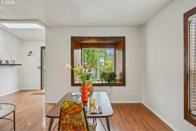 dining space featuring baseboards, wood finished floors, and a skylight