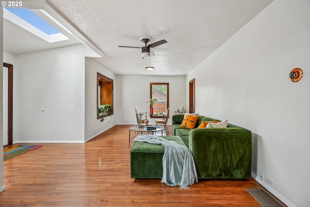 living area featuring wood finished floors, baseboards, ceiling fan, a textured ceiling, and a skylight