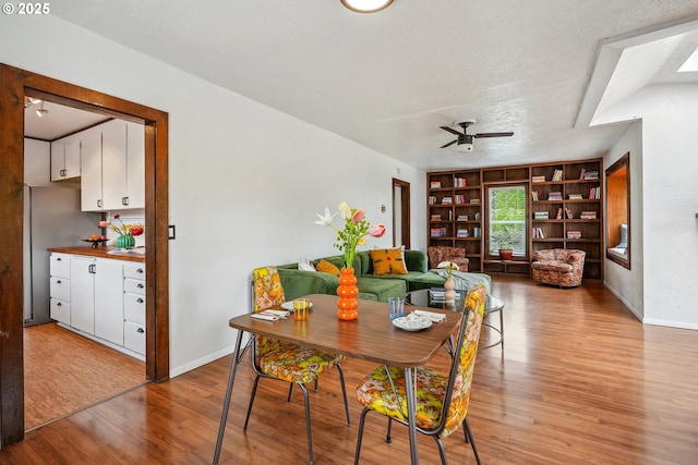 dining room featuring built in features, baseboards, a ceiling fan, and light wood finished floors