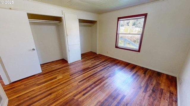 unfurnished bedroom with dark hardwood / wood-style flooring and two closets