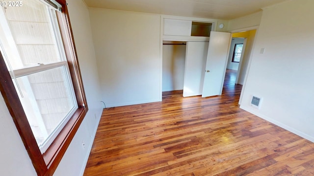 unfurnished bedroom with wood-type flooring, ornamental molding, and a closet