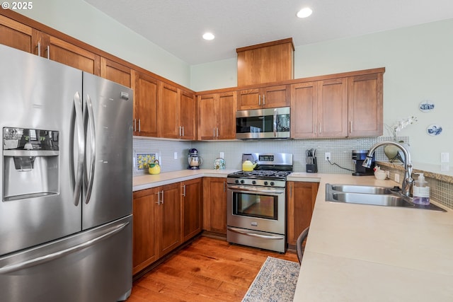 kitchen with stainless steel appliances, light wood-type flooring, light countertops, and a sink