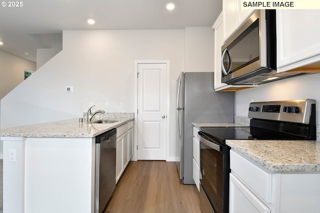 kitchen with light wood finished floors, a peninsula, a sink, white cabinets, and appliances with stainless steel finishes