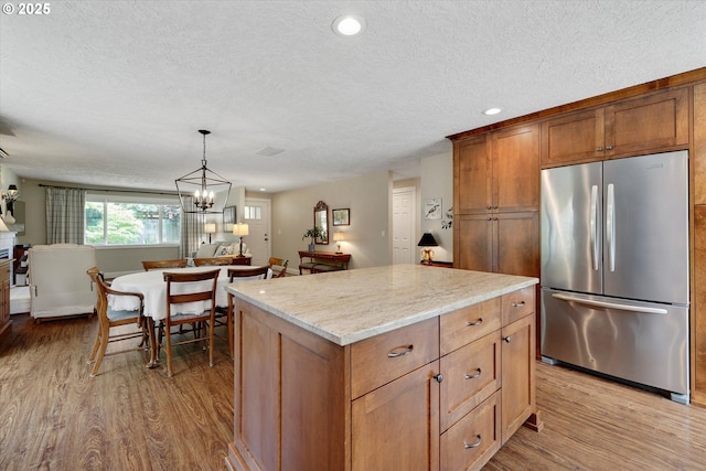 2648 SE Risley Ave, Milwaukie, OR 97267 - kitchen with stainless steel fridge, wood finished floors, a textured ceiling, a center island, and decorative light fixtures