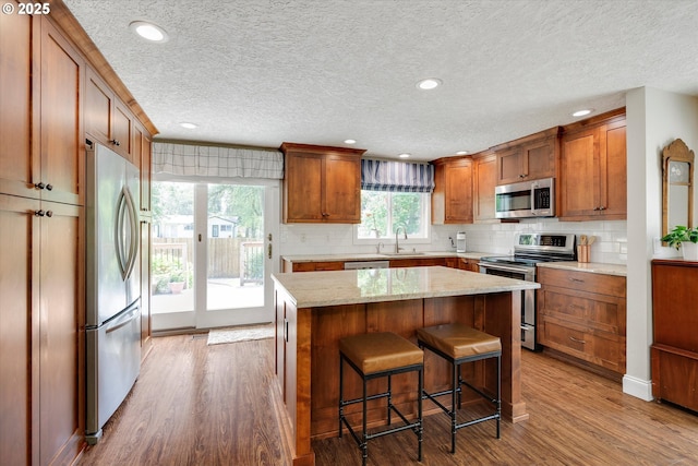 2648 SE Risley Ave, Milwaukie, OR 97267 - kitchen featuring stainless steel appliances, wood finished floors, tasteful backsplash, brown cabinets, and a textured ceiling