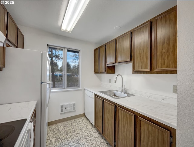 kitchen featuring baseboards, light stone counters, white appliances, visible vents, and a sink
