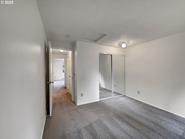 unfurnished bedroom featuring baseboards, a closet, carpet flooring, a textured ceiling, and attic access