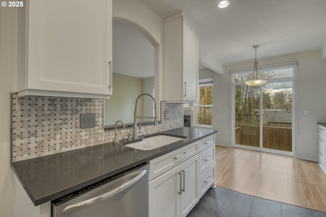 kitchen with a sink, dark countertops, dishwasher, and white cabinets