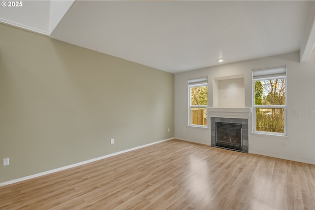 unfurnished living room with a tiled fireplace, light wood-style flooring, and baseboards