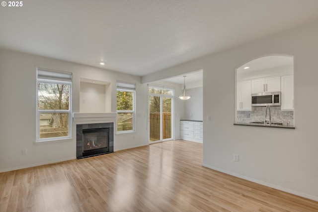 unfurnished living room with a wealth of natural light, light wood finished floors, baseboards, and a tile fireplace