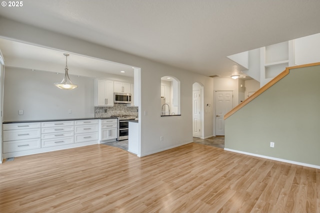 unfurnished living room with baseboards, arched walkways, visible vents, and light wood finished floors