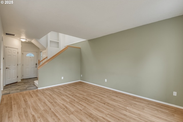 unfurnished living room with light wood-type flooring, visible vents, baseboards, and stairway