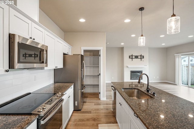 kitchen with dark stone counters, appliances with stainless steel finishes, decorative light fixtures, white cabinetry, and a sink