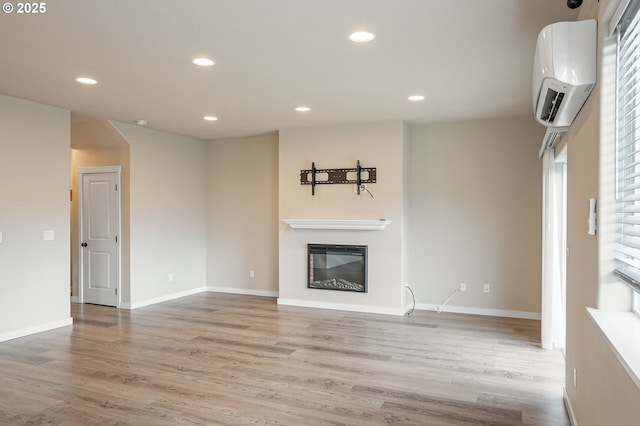 unfurnished living room featuring baseboards, a glass covered fireplace, wood finished floors, a wall mounted air conditioner, and recessed lighting