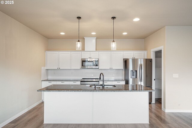 kitchen featuring stainless steel appliances, a kitchen island with sink, white cabinets, and backsplash