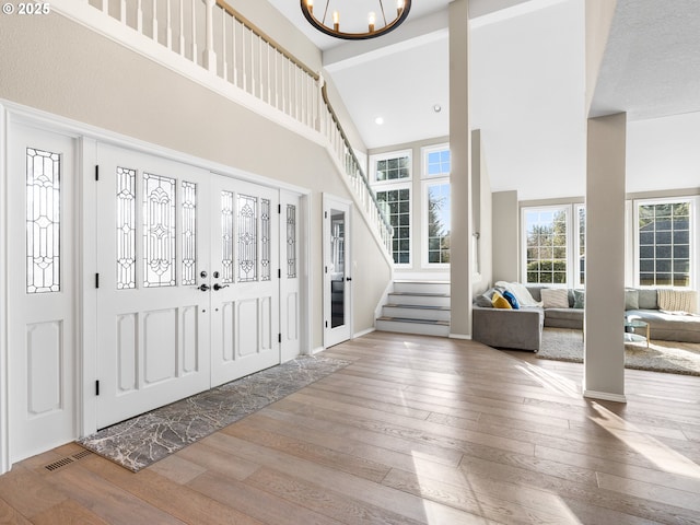 entryway with a towering ceiling, an inviting chandelier, light wood-style flooring, and stairway