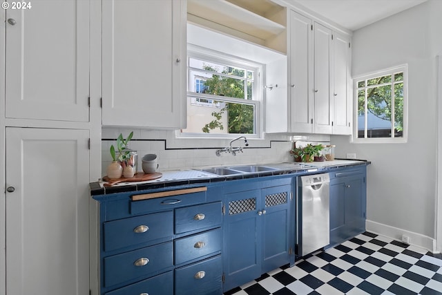 kitchen with tile patterned floors, stainless steel dishwasher, blue cabinets, a sink, and white cabinetry