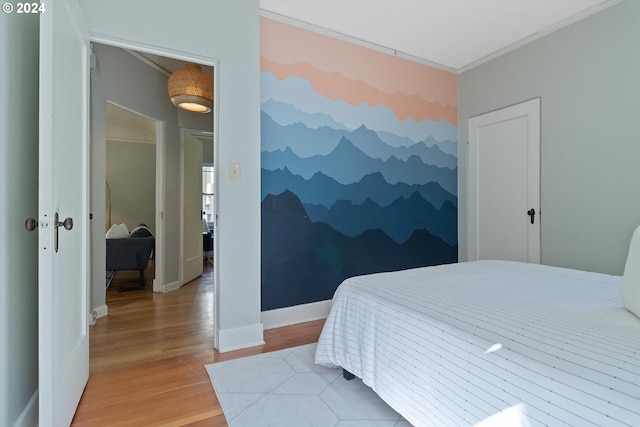 bedroom with light wood-style floors, an accent wall, baseboards, and ornamental molding