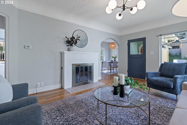 living room featuring arched walkways, a textured ceiling, a notable chandelier, wood finished floors, and a textured wall
