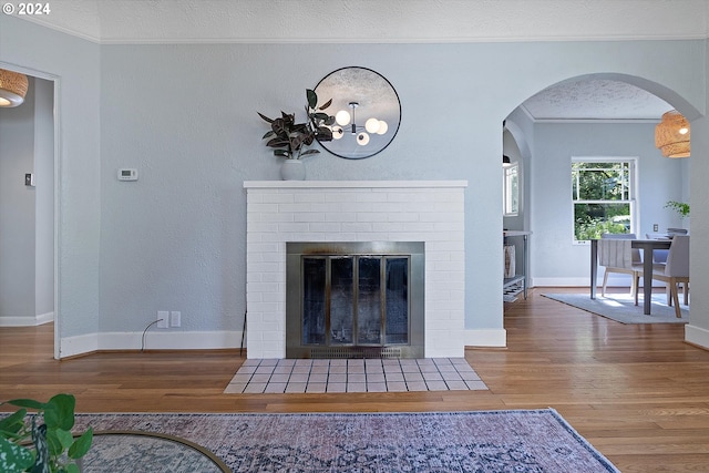living area featuring arched walkways, wood finished floors, a brick fireplace, and ornamental molding