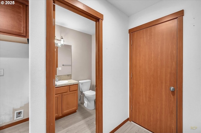 bathroom with toilet, wood finished floors, vanity, and baseboards