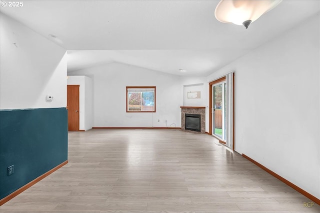 unfurnished living room with a healthy amount of sunlight, light wood-style floors, lofted ceiling, and a high end fireplace