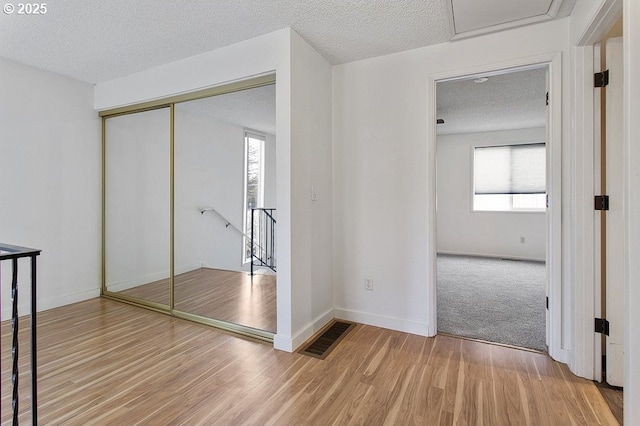 hallway with an upstairs landing, wood finished floors, a textured ceiling, and baseboards