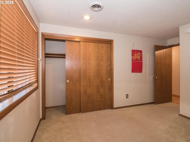 unfurnished bedroom with light carpet, a textured ceiling, and a closet