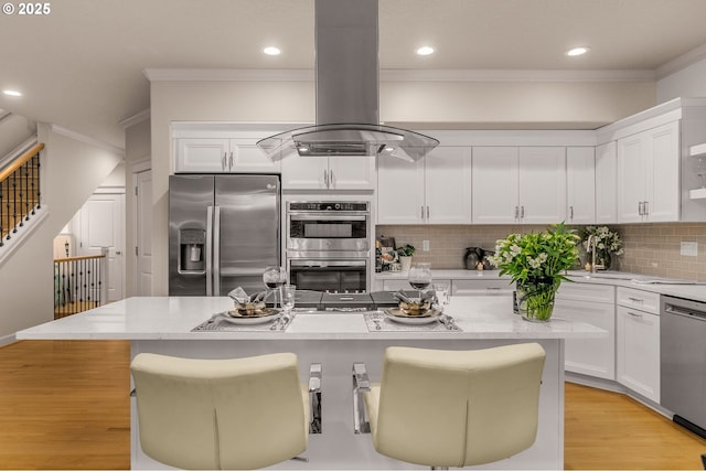 kitchen with stainless steel appliances, island exhaust hood, crown molding, white cabinetry, and a breakfast bar