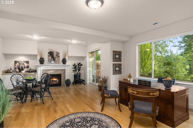 home office featuring light wood finished floors, plenty of natural light, a tile fireplace, and a textured ceiling