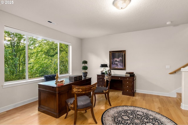 office area featuring baseboards, light wood-type flooring, and a textured ceiling