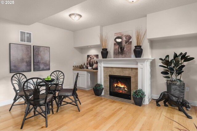 dining room featuring wood finished floors, a tiled fireplace, baseboards, and a textured ceiling