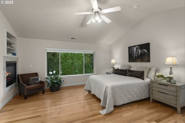 bedroom with lofted ceiling, light wood-style flooring, a fireplace, a ceiling fan, and baseboards