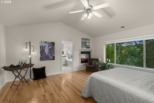 bedroom featuring vaulted ceiling, light wood-style floors, a tile fireplace, connected bathroom, and baseboards