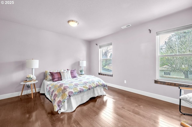 bedroom with hardwood / wood-style flooring, visible vents, and baseboards