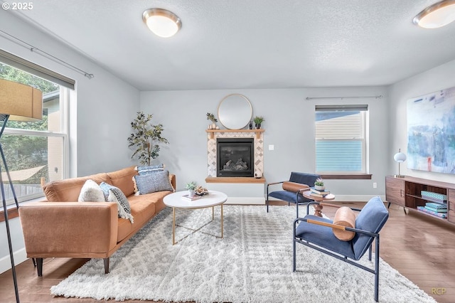 living room featuring a textured ceiling, baseboards, wood finished floors, and a high end fireplace